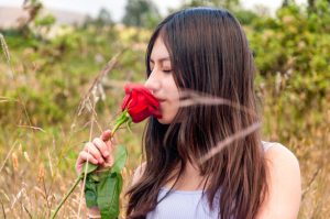 Teenage-girl-smelling-a-red-rose-in-a-field-2190788809_728x483-1-300x199